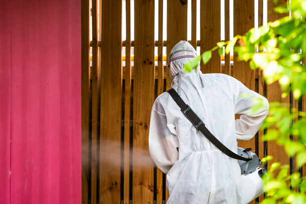 Hombre técnico profesional en traje de prevención con su máquina esterilizadora y pulverizadores de agua desinfectantes en el campo exterior para la purificación del coronavirus (COVID-19). - Foto, imagen