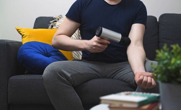 Brazo de masaje de hombre con dispositivo de percusión de masaje en casa. - Foto, imagen