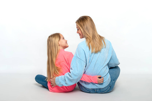 Szőkék fotózása, anya és lánya rózsaszín ingben, ahogy ölelkeznek, és szívformát öltenek rózsaszín alapon, visszapillantás - Fotó, kép