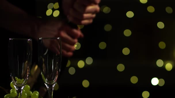 Oříznout pohled na mužské ruce otevírající láhev šampaňského a nalévající ji do dvou sklenic - Záběry, video