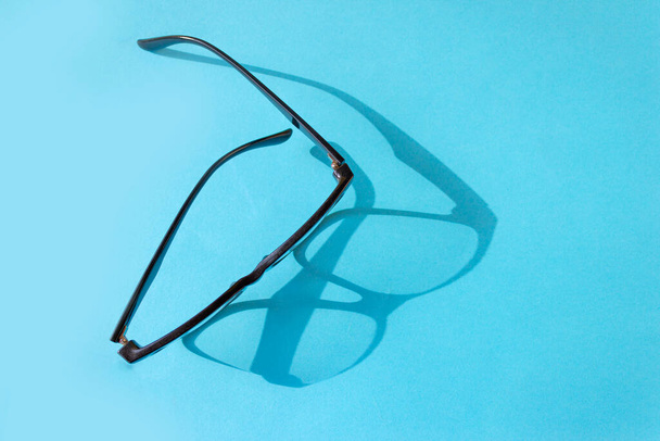 青い背景に黒い枠の眼鏡。メガネからのハードシャドウ。ビジョンコンセプト. - 写真・画像