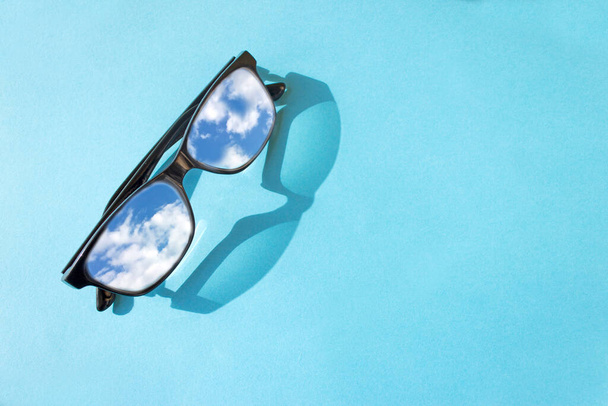 Brille mit schwarzem Rahmen auf blauem Hintergrund. Das Konzept des Sehens, die Reflexion des Himmels in den Brillengläsern. - Foto, Bild