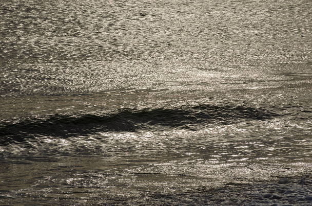 Jogo de raios de sol na superfície da água. A onda do mar está se movendo em direção à costa - Foto, Imagem