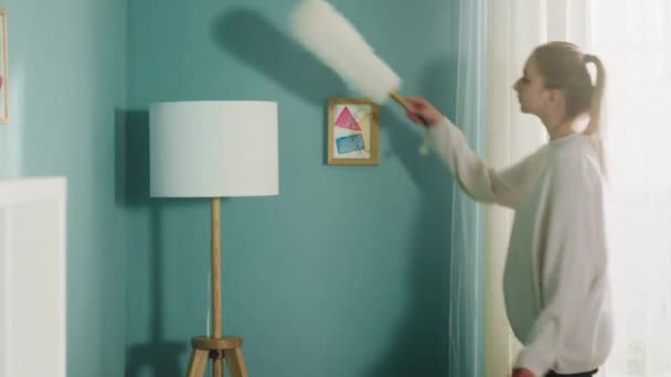 Mujer joven en suéter blanco limpia el polvo de los muebles. - Metraje, vídeo