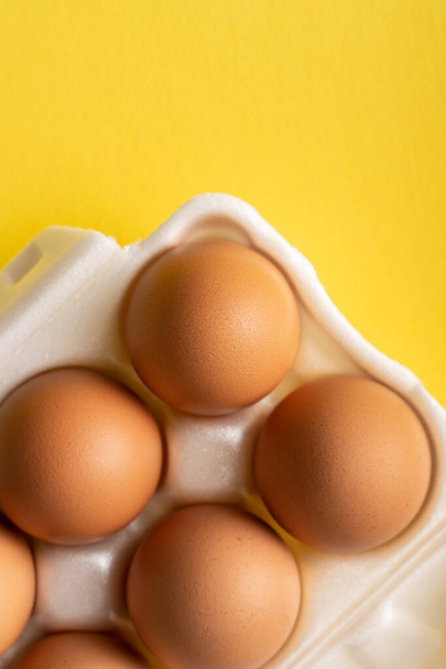 Top view tuoreita orgaanisia munia laatikossa kontti keltaisella pohjalla - Valokuva, kuva