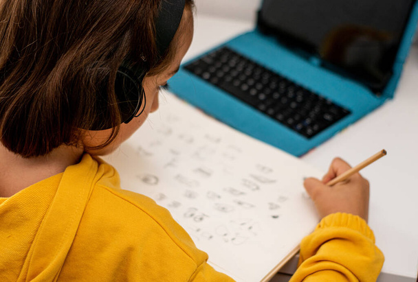 Detailaufnahme eines Mädchens mit Gips in der einen Hand, das einen gelben Pullover trägt und Skizzen in ihrem Skizzenbuch, auf ihrem Schlafzimmertisch, mit Zeichenmaterial und einem Tablet zeichnet.. - Foto, Bild