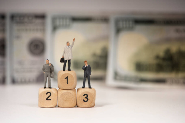 Мініатюрна фігура людей бізнесмен стоїть на дерев'яному блоці з банкнотою долара, бізнес-концепція
 - Фото, зображення