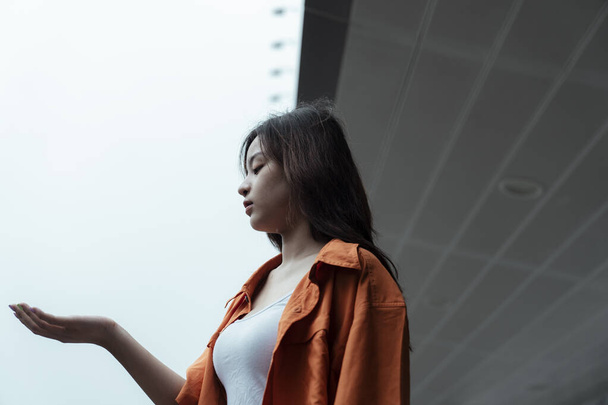 Oranžová košile dívka stojící u markýzy nákupního centra, uvolněte její ruku, aby zkontrolovala déšť. - Fotografie, Obrázek