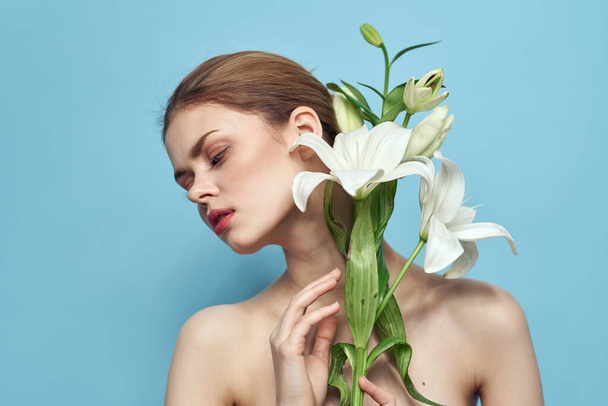 Belle fille avec un bouquet de fleurs blanches sur un fond bleu vue recadrée épaules nues portrait - Photo, image