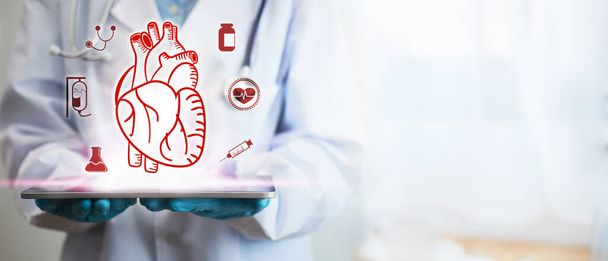 Concept of treatment for heart disease. A doctor's hand is holding a tablet showing a heart icon, along with the background is a picture of blurred with light. - Photo, Image