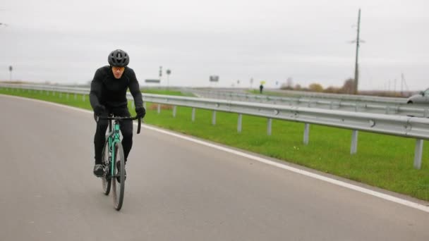 De sporter traint op de fiets. Hij rijdt op de snelweg in het koude seizoen. 4K - Video