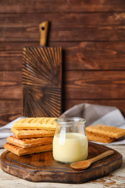 Βάζο με γλυκό συμπυκνωμένο γάλα και βάφλες σε ξύλινο φόντο - Φωτογραφία, εικόνα