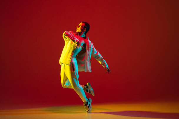 Joven bailarín bailando hip-hop aislado sobre fondo rojo en luz de neón - Foto, Imagen