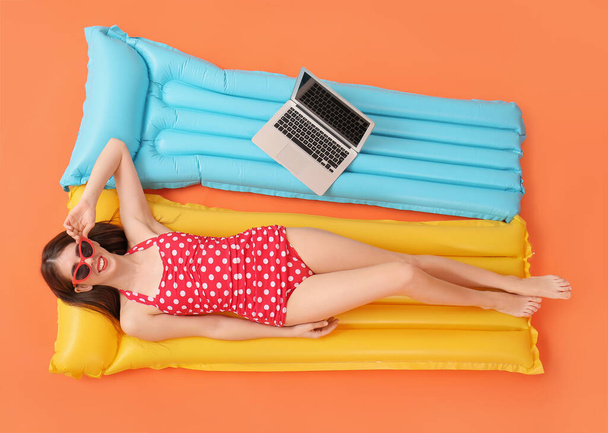 Beautiful woman with laptop lying on inflatable mattress against color background - Photo, Image