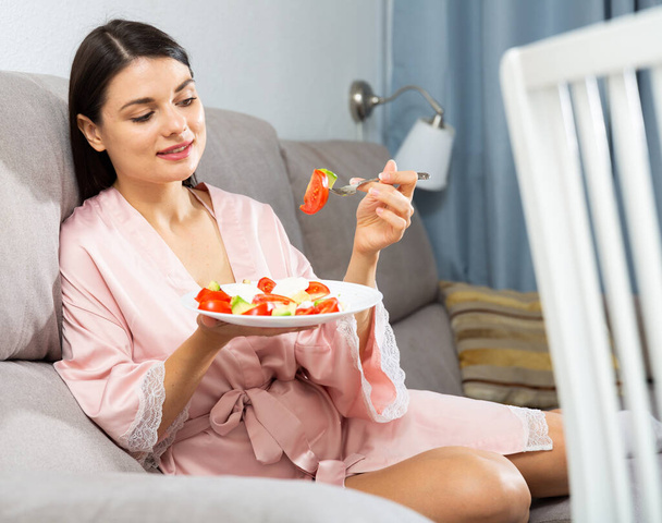 Satisfied woman sitting on sofa at home and eating healthy food - Zdjęcie, obraz