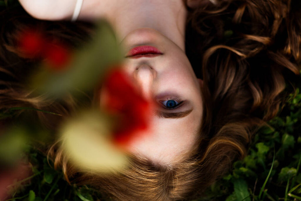 Πάνω από την εικόνα ενός όμορφου κοριτσιού με κόκκινα σγουρά μαλλιά και μπλε μάτια, κοιτάζοντας την κάμερα. Καλλιτεχνική ιδέα για φθινοπωρινά χρώματα. - Φωτογραφία, εικόνα