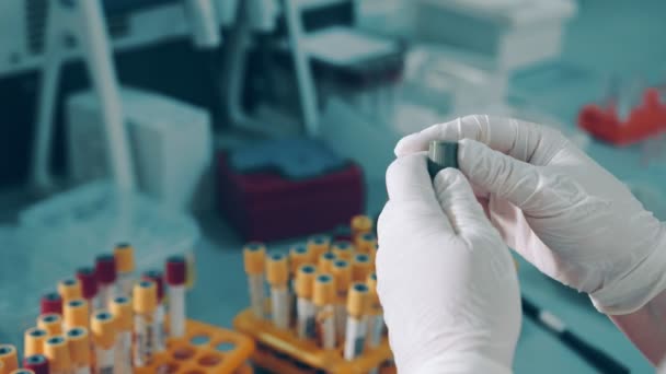 Close up de um assistente de laboratório segurando um tubo de ensaio com sangue infectado com coronavírus covid19 e uma pipeta doseadora de sangue de bétula para análise em laboratório. - Filmagem, Vídeo