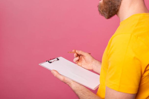 Young bearded employee man casual wear taking notes against a pink background - Foto, imagen