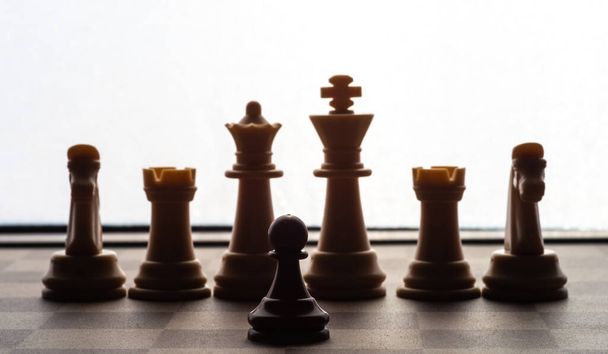 kleine pion op schaakbord tegen grotere tegenstander begrip van tegenslag, disciminatie, gelijkheid .focus op de grond - Foto, afbeelding