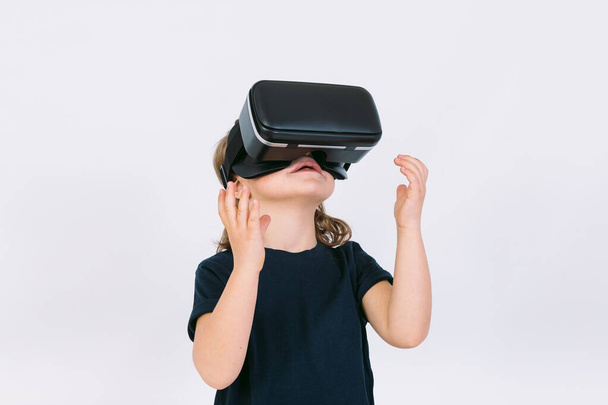 Niña con gafas de realidad virtual mirando hacia arriba sobre fondo blanco - Foto, imagen