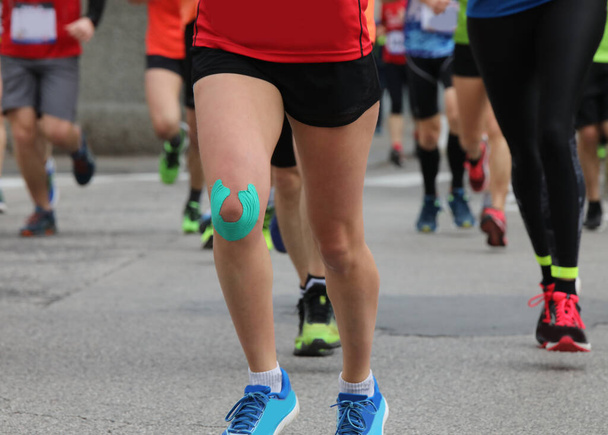 молодой бегун во время гонки на ноге с бинтом на колене, чтобы избежать мышечного напряжения - Фото, изображение