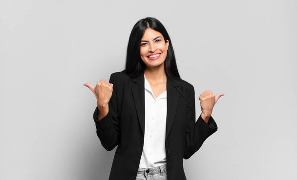 young hispanic businesswoman smiling joyfully and looking happy, feeling carefree and positive with both thumbs up - Photo, image