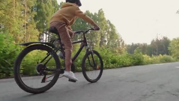 Seguimiento de la vista lateral de plano completo de deportista de 12 años de edad, chico caucásico en bicicleta casco en el sendero en el parque entre los árboles en el día soleado - Imágenes, Vídeo