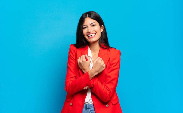 young hispanic businesswoman smiling cheerfully and celebrating, with fists clenched and arms crossed, feeling happy and positive - 写真・画像