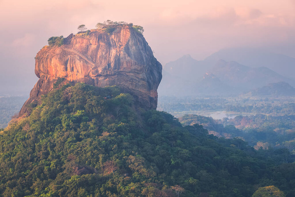 Pohled do džungle na starobylou skalní pevnost Sigiriya z kopce Pidurangala na Srí Lance s barevným západem slunce nebo východem slunce. - Fotografie, Obrázek