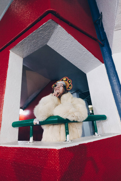 a beautiful girl in white fur coat and crown posing on the balcony - Valokuva, kuva