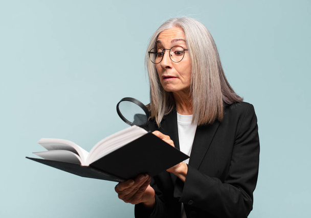 Una mujer guapa mayor con un libro y una lupa. concepto de búsqueda - Foto, Imagen