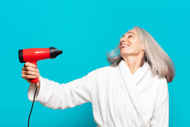 Duştan sonra bornoz giyen yaşlı ve güzel bir kadın. Saç kurutma makinesi konsepti - Fotoğraf, Görsel