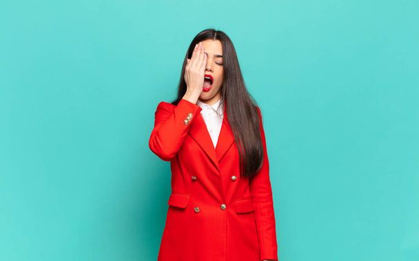 young pretty woman looking sleepy, bored and yawning, with a headache and one hand covering half the face. business concept - 写真・画像