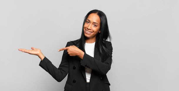 young black woman smiling, feeling happy, carefree and satisfied, pointing to concept or idea on copy space on the side. business concept - Photo, image