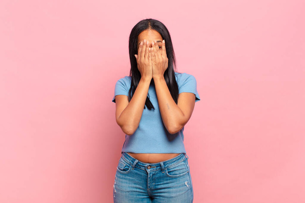 young black woman covering face with hands, peeking between fingers with surprised expression and looking to the side - Foto, imagen