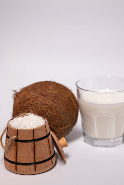 frische Kokosnuss in der Nähe von Holzschüssel mit Kokosflocken und einem Glas Kokosmilch. isoliert auf weißem Hintergrund. Tropische Nuss. - Foto, Bild
