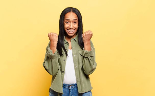 jonge zwarte vrouw schreeuwen triomfantelijk, lachen en het gevoel gelukkig en opgewonden terwijl het vieren van succes - Foto, afbeelding