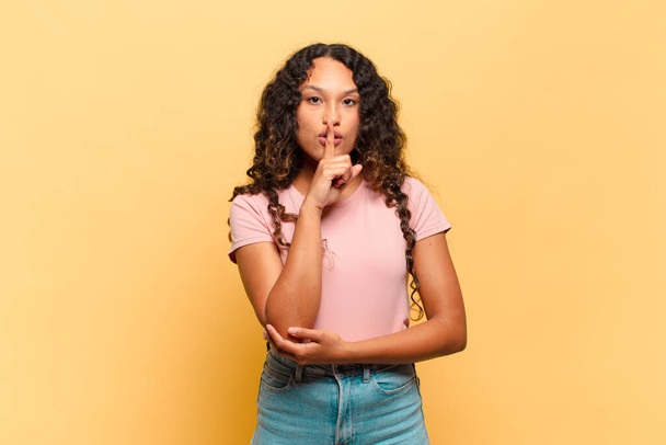 young hispanic woman looking serious and cross with finger pressed to lips demanding silence or quiet, keeping a secret - Foto, afbeelding