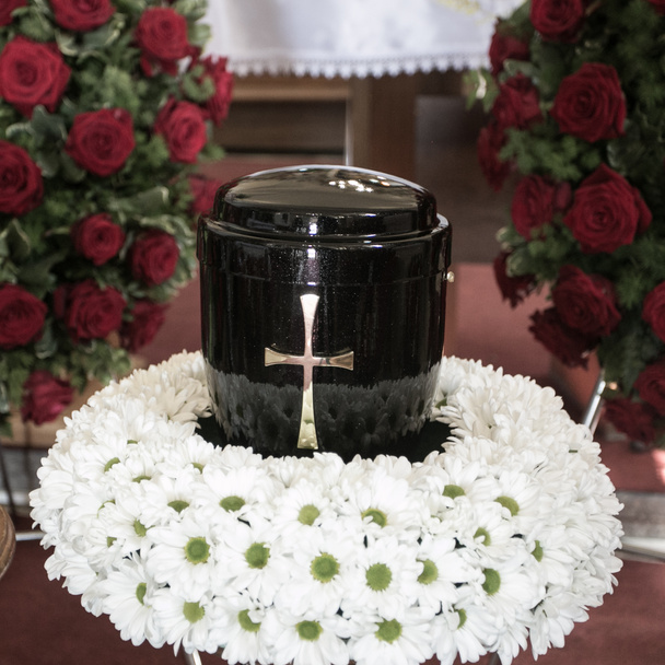 Fekete urna a temetés napján a templomban; körülvéve százszorszépekkel és rózsákkal - Fotó, kép