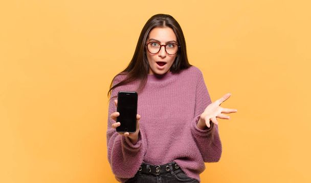 young pretty woman feeling extremely shocked and surprised, anxious and panicking, with a stressed and horrified look. phone screen concept - Zdjęcie, obraz