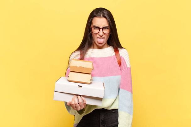 young pretty woman feeling disgusted and irritated, sticking tongue out, disliking something nasty and yucky. take aeay fast food concept - 写真・画像