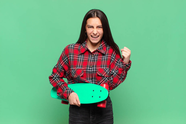 young pretty woman feeling shocked, excited and happy, laughing and celebrating success, saying wow!. skate board concept - Foto, Bild