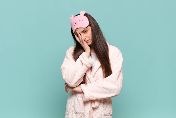 young pretty woman feeling bored, frustrated and sleepy after a tiresome, dull and tedious task, holding face with hand. awaking wearing pajamas concept - Foto, imagen
