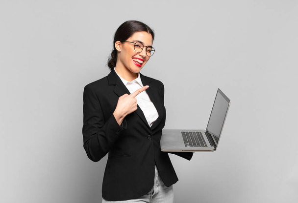 young pretty woman looking excited and surprised pointing to the side and upwards to copy space. laptop concept - Photo, image