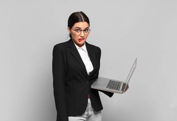 young pretty woman looking puzzled and confused, biting lip with a nervous gesture, not knowing the answer to the problem. laptop concept - Foto, imagen