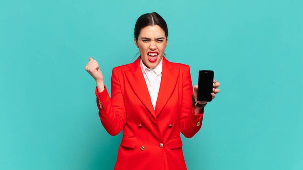 young pretty woman shouting aggressively with an angry expression or with fists clenched celebrating success. smart phone concept - Zdjęcie, obraz