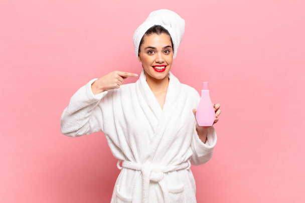 young pretty woman smiling confidently pointing to own broad smile, positive, relaxed, satisfied attitude. bathrobe and face cleaning concept - Fotoğraf, Görsel