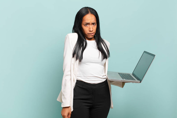 young black woman looking puzzled and confused, biting lip with a nervous gesture, not knowing the answer to the problem. laptop concept - Photo, image