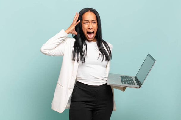 young black woman screaming with hands up in the air, feeling furious, frustrated, stressed and upset. laptop concept - Photo, image
