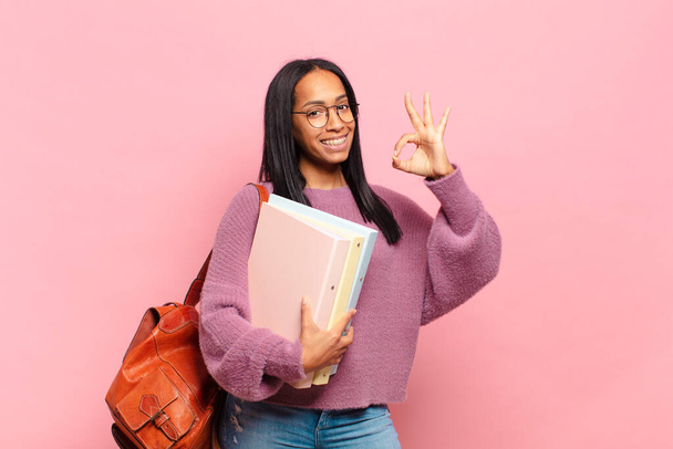 joven mujer negra sintiéndose feliz, relajada y satisfecha, mostrando aprobación con gesto bien, sonriendo. concepto de estudiante - Foto, imagen